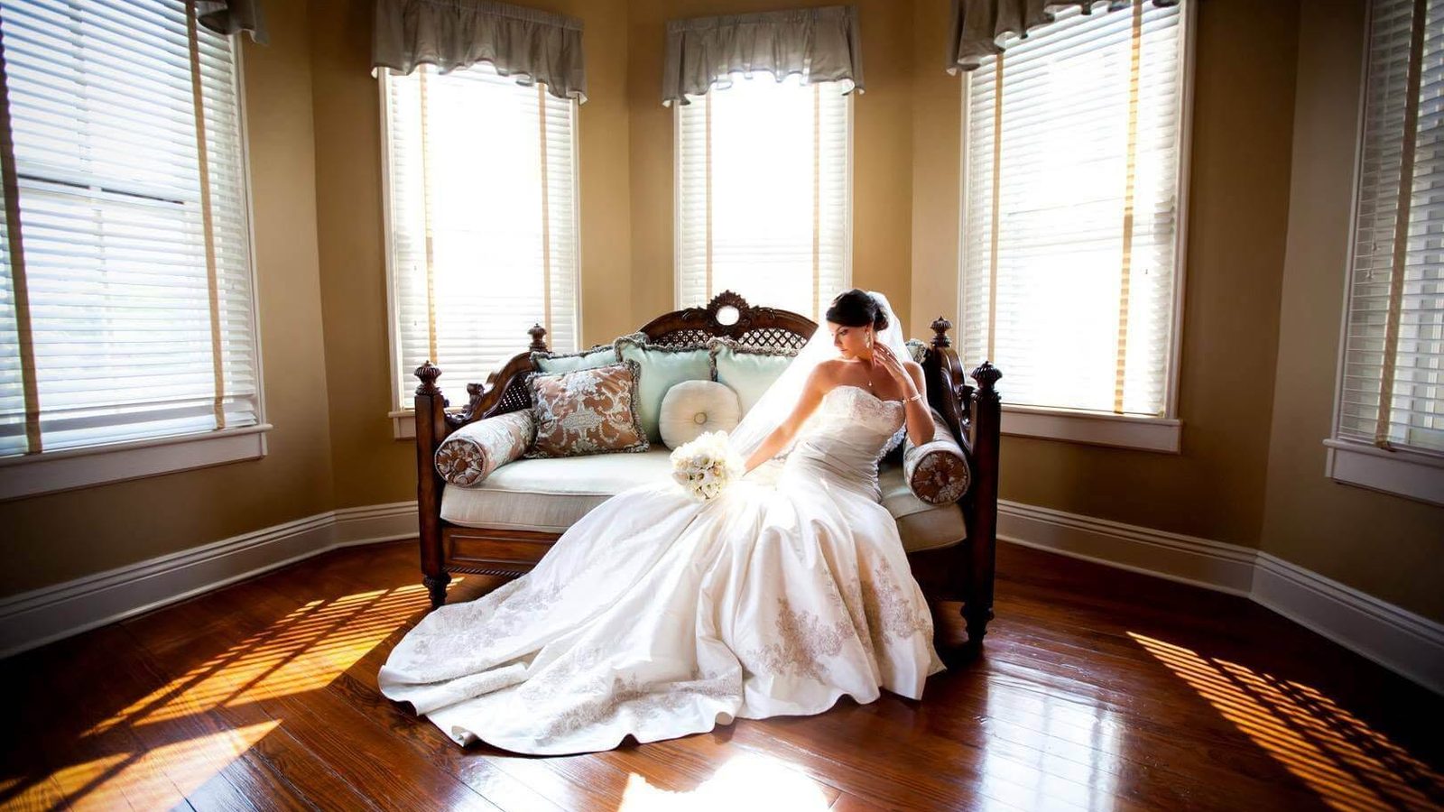 A bride seated on an antique daybed in the sunlit bay-window bridal suite of The Caldwell House