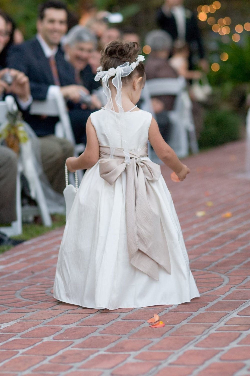 A flower girl walking the brick aisle at an outdoor wedding ceremony at The Caldwell House as seated guests look on