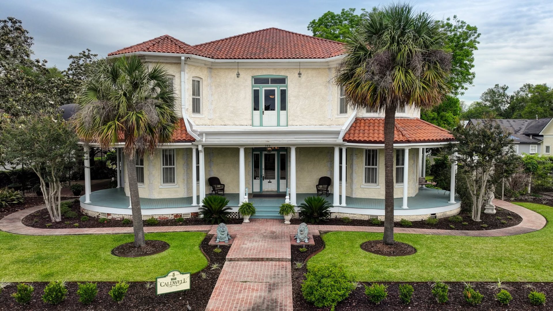The Caldwell House, a historic two-story estate with a wraparound porch and palm-lined brick walkway in downtown Abbeville, Louisiana