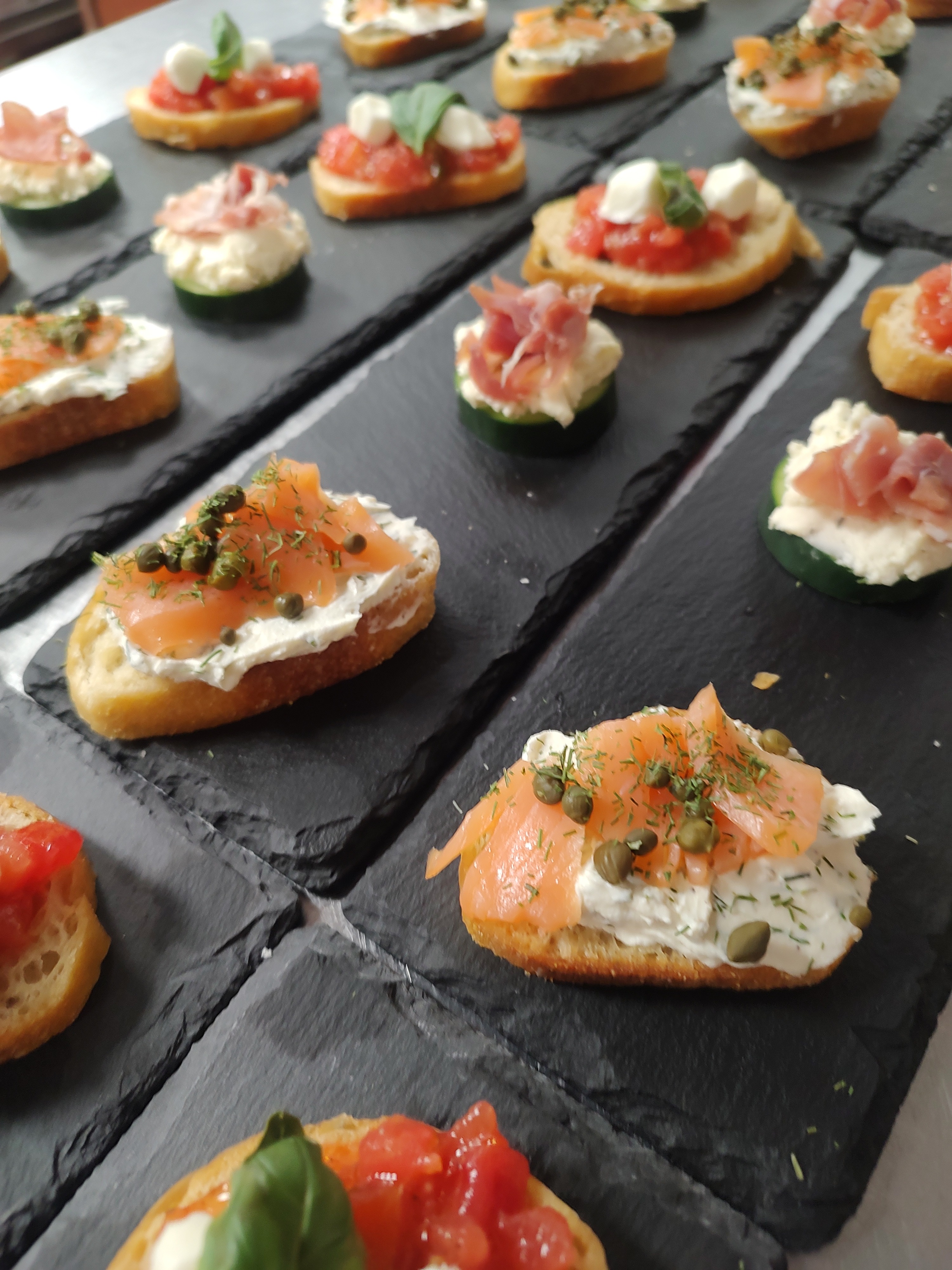 Smoked salmon and dill crostini, tomato bruschetta, and prosciutto and cucumber canap&eacute;s arranged on slate boards by The Southern Spread