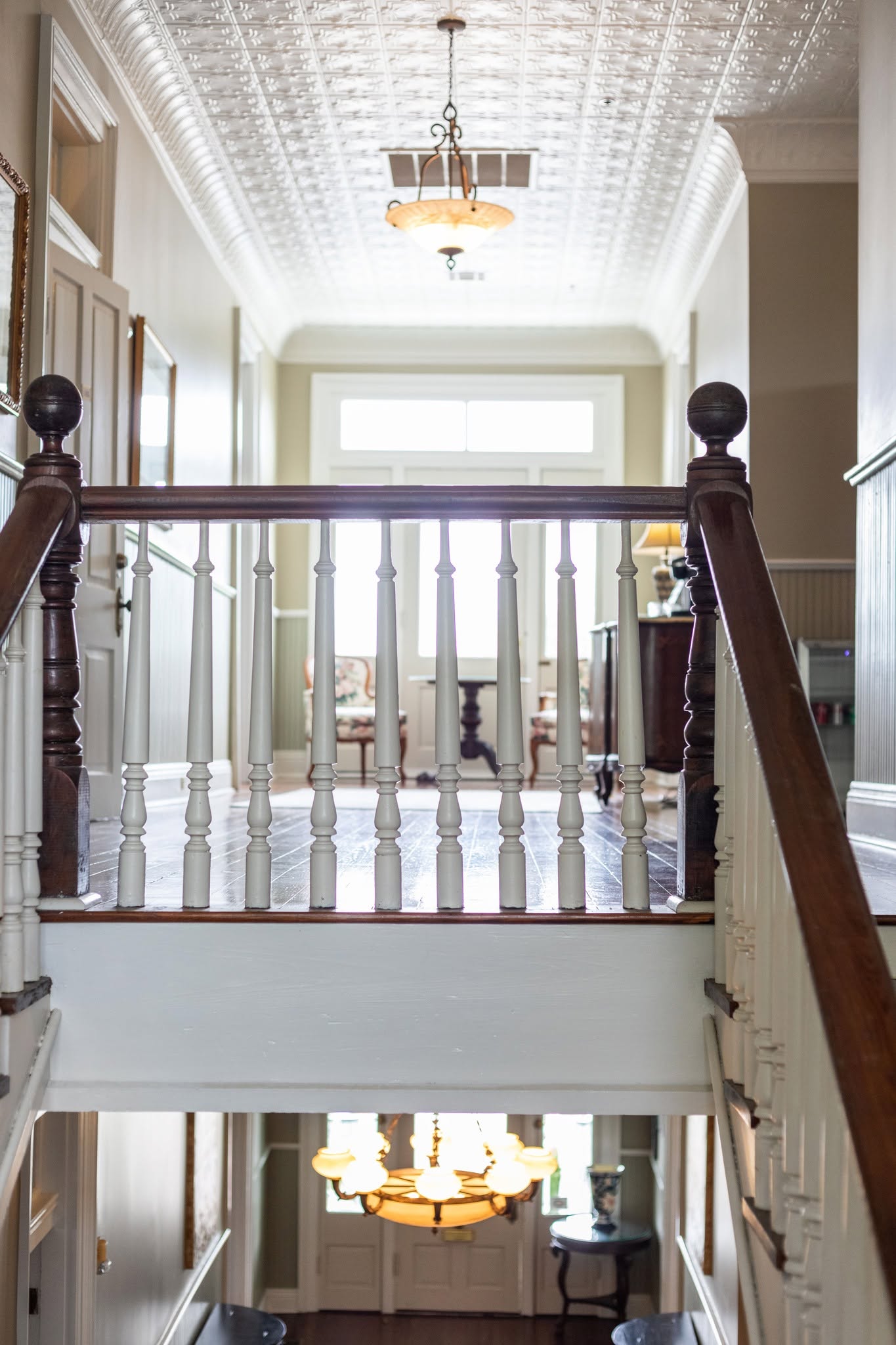 An upstairs landing at The Caldwell House with turned balusters, a pressed-tin ceiling, and heart-pine floors