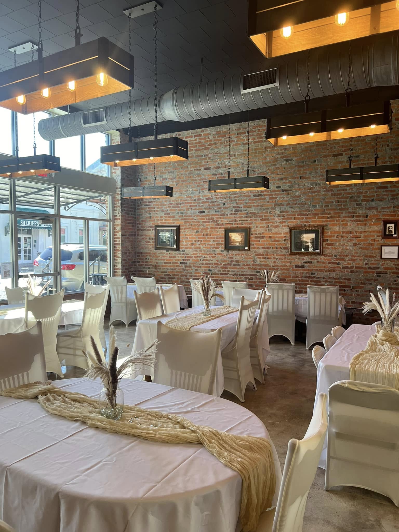 The Russo set for a celebration with white linens, pampas grass runners, and framed art on the original 1914 brick wall